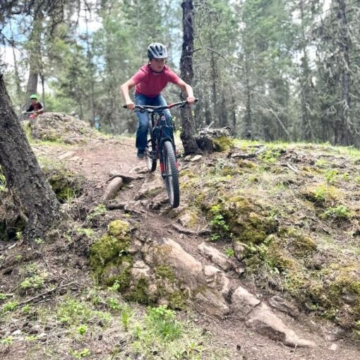 A youth confidently rides their bicycle down a rocky and rooty section of trail