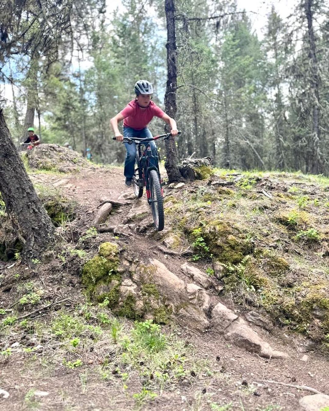 A youth confidently rides their bicycle down a rocky and rooty section of trail